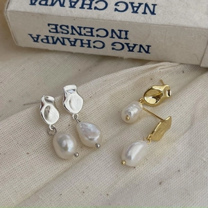 Detailed macro of gold and silver baroque pearl earrings on beige linen fabric background