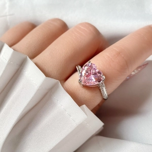Primer plano de un anillo de cristal rosa con forma de corazón y banda de plata en el dedo