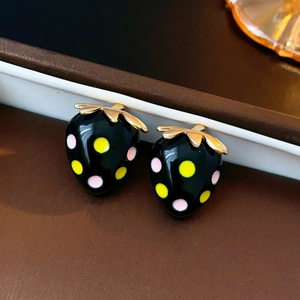 Détail macro de boucles d'oreilles fraises noires à pois roses et feuilles dorées