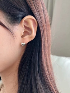 Detail of heart-shaped silver stud earring with monogram engraving on model's ear