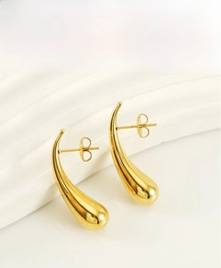 Detailed macro view of gold-plated teardrop earrings on white textured marble display