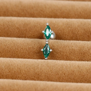 Detail of silver cartilage stud with two marquise-cut green zircons on a brown tray