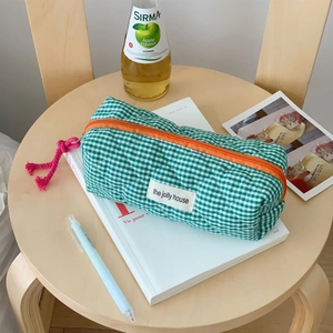 Detail of green checkered quilted pouch with orange zipper and pink tassel on a table