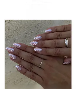 Détail de faux ongles amande courts avec base rose nacrée et motifs à pois blancs