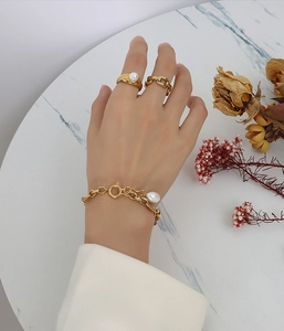 Detail of 18k gold plated chain bracelet with pearl pendant and vintage stackable rings