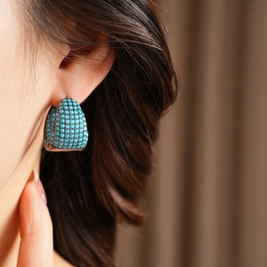 Close-up of model wearing turquoise pavé C-shaped hoop earrings in silver metal