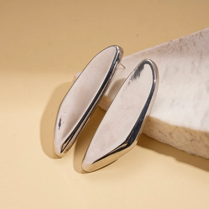 Macro detail of polished irregular silver-tone metal earrings on a textured stone base