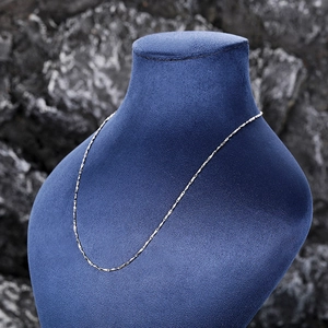 Silver thin chain necklace displayed on blue velvet bust with dark rock background