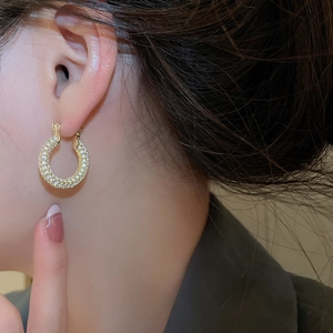Close-up of model wearing gold-plated U-shaped hoop earrings with sparkling zircons