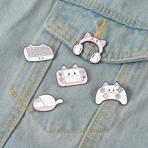Close-up of pink cat-themed gaming enamel pins displayed on blue denim fabric