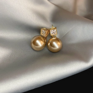 Macro shot of gold square zircon studs with pearls on elegant silver silk fabric