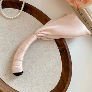 Détail d'une pince à cheveux banane en satin rose clair sur un plateau en bois