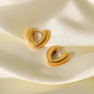 Macro view of polished 18K gold plated heart hoop earrings on beige silk fabric