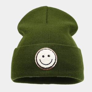 Dettaglio del berretto in maglia verde scuro con toppa ricamata a sorriso