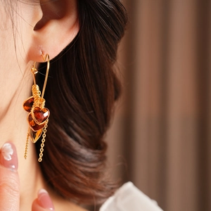 Macro detail of 18K gold-plated earrings with amber heart pendants and chain tassels