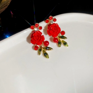 Macro detail of red rose earrings with sparkling crystals and green enamel leaf accents