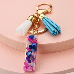 Detail of a gold keychain with blue and white tassels and colorful resin stone pendant