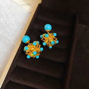 Detail of flower stud earrings with sky blue beads and gold metal frame on brown velvet