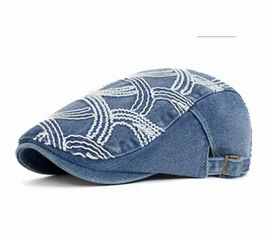 Detail of blue denim beret with white stitching embroidery and metal buckle adjustment