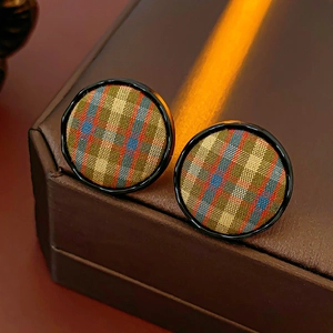 Macro detail of round plaid fabric earrings with polished black frames in retro style