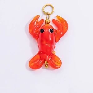 Detailed view of an orange glass lobster charm with an 18k gold-plated metal loop