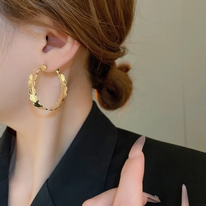 Close-up of golden wavy hoop earrings showing detailed metallic texture on model