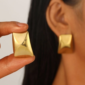 Detail of a geometric gold rectangular stud earring shown on ear and held by hand
