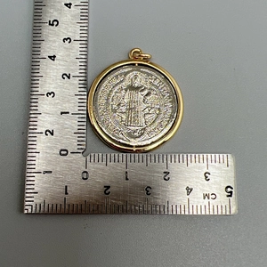 Macro shot of gold and silver religious cross pendant showing a 2.5cm diameter on ruler