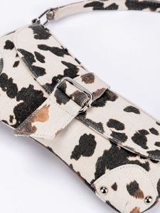 Cow print canvas shoulder bag with asymmetric saddle shape and silver buckle detail