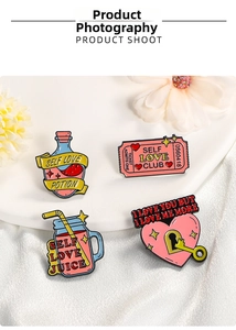 Detail of four enamel pins with pastel self-love themes on a white display stand