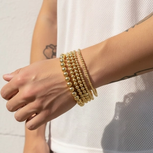 Detail of 18K gold-plated beaded stretch bracelets with five graduated sizes on a wrist