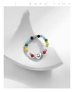 Gros plan d'une bague en perles colorées avec breloque cœur smiley argenté sur céramique