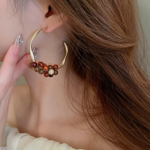 Side view of model wearing large C-shaped gold hoop earrings with brown wooden beads