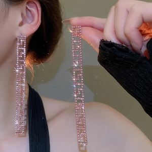 Dettaglio di orecchini con nappe di strass rosa e motivo geometrico greco su modella