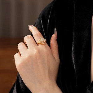 Gros plan d'une bague fleur dorée avec perles et petits diamants sur un doigt