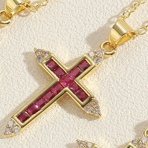 Macro detail of 14K gold plated cross pendant with red crystals and white cubic zirconia