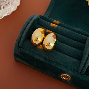 Macro shot of polished gold oval hoop earrings inside a dark green velvet jewelry box