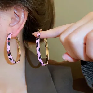 Pink leopard print hoop earrings with gold inner lining worn by a model in a close-up