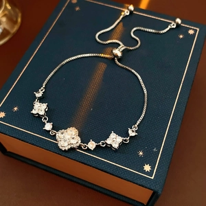 Macro detail of silver clover bracelet with zircon inlay on luxury navy gift box