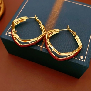 Close-up of geometric gold earrings with reddish-brown enamel on a blue gift box