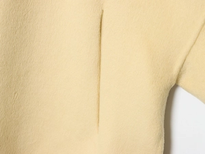 Macro view of light yellow wool blend fabric texture and detailed stitching on the coat