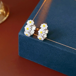 Close-up of vintage enamel daisy hoop earrings on a textured blue gift box background