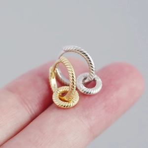 Macro shot of silver and gold mini hoop earrings with twisted texture on a fingertip