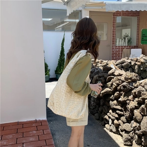 Close-up of cream canvas shoulder bag with floral lace patterns in outdoor setting