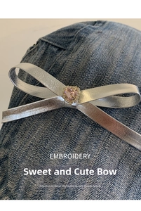 Detail of silver metallic bow accessory with a pink heart gemstone on denim