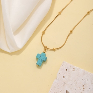 Gold-plated necklace with turquoise cross pendant and beaded chain on elegant fabric