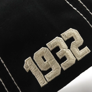 Macro shot of 1932 numeric embroidery and white stitching on black cotton baseball cap