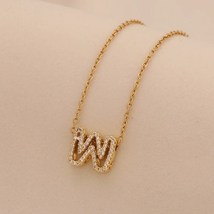 Macro detail of a gold letter W pendant necklace with clear sparkling zircon stones