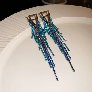 Dettaglio degli orecchini geometrici con nappe di strass blu sfumati su piatto di ceramica