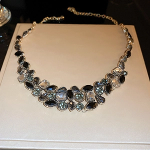 Detail of bib style necklace with black and teal crystals set in gold metal